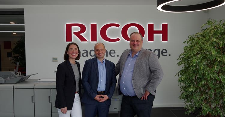Nicole Schneider, National Director Sales Public Account Division bei Ricoh Deutschland GmbH, Enrico Kropfgans, Manager Business Development bei der PDV GmbH & Ingo Wittrock, Regional Director Marketing Central & Eastern Europe bei Ricoh stehen gemeinsam vor dem Ricoh Logo